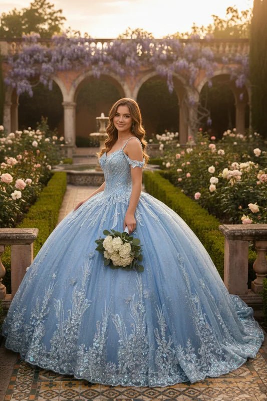 Young woman in blue off-the-shoulder lace ball gown with floral embroidery, standing in a garden holding white bouquet.